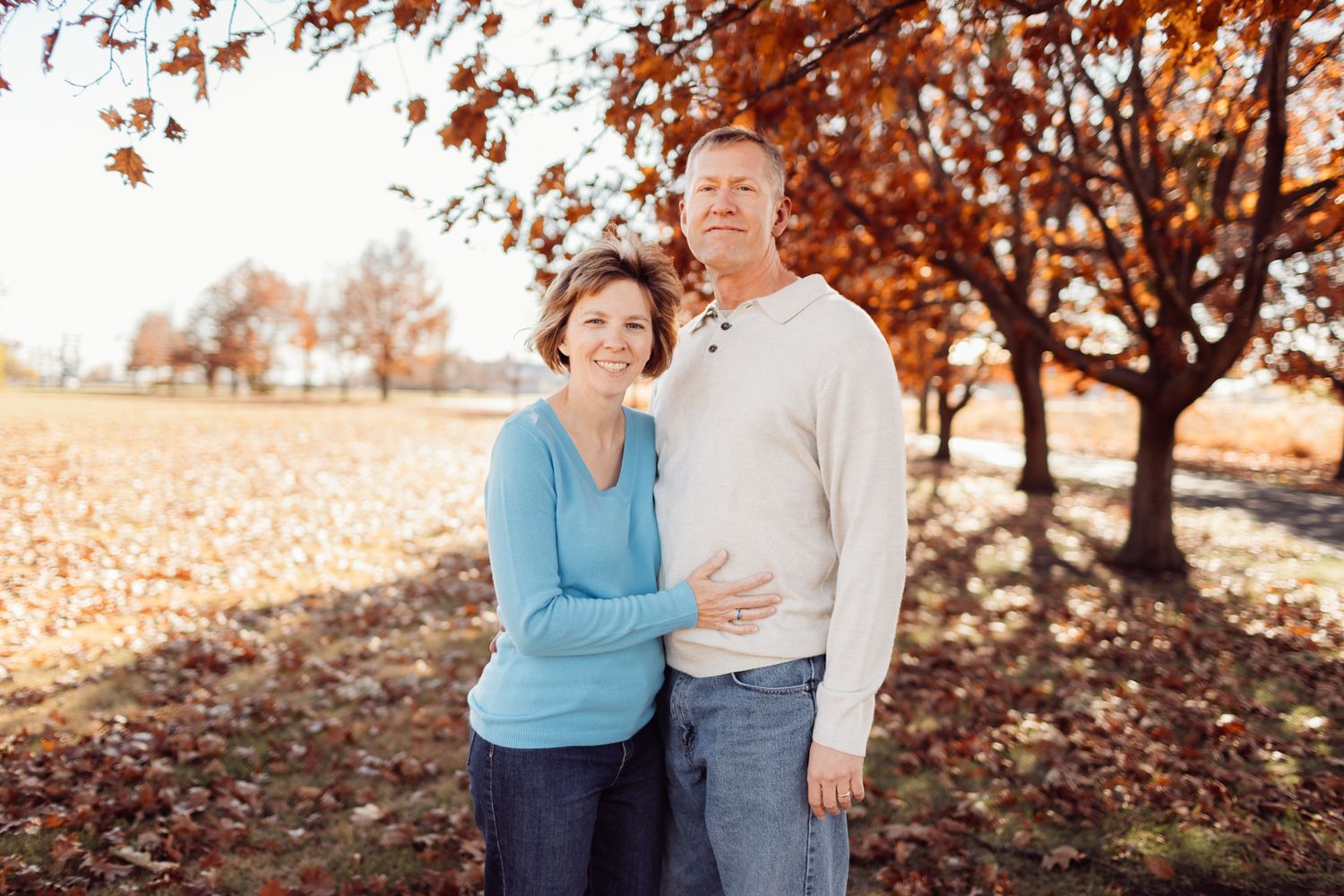 Middle-aged couple embracing under vibrant autumn foliage in a park setting.