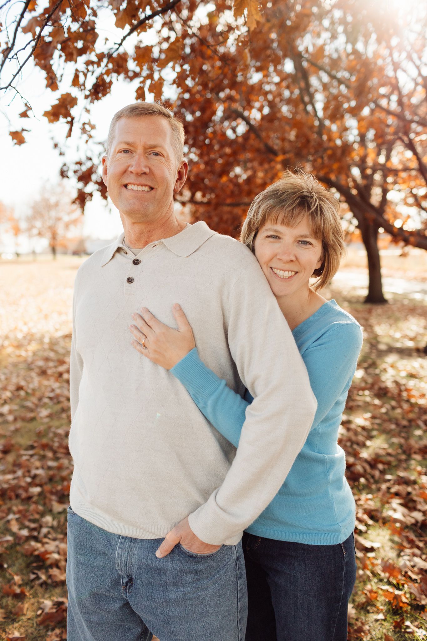 Smiling couple posing together under colorful fall trees in warm sunlight.
