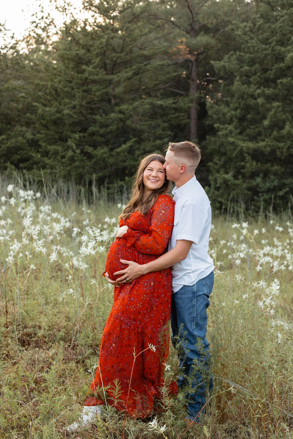 Couple sharing a tender moment in a wildflower field, woman in red floral maternity dress.