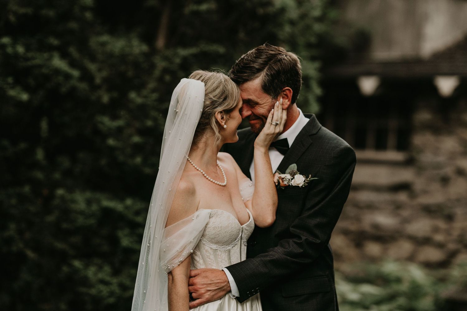bride gently touching grooms face as he smiles holding her in an embrace.