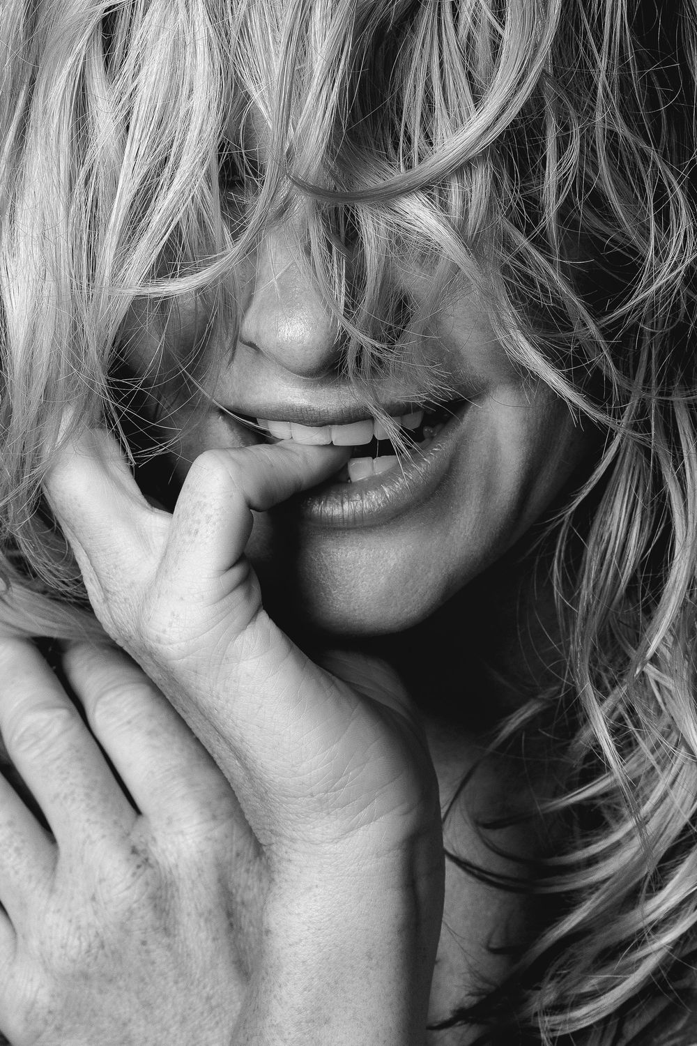 A black and white artistic portrait showing blonde wavy hair and a hand partially covering the face.
