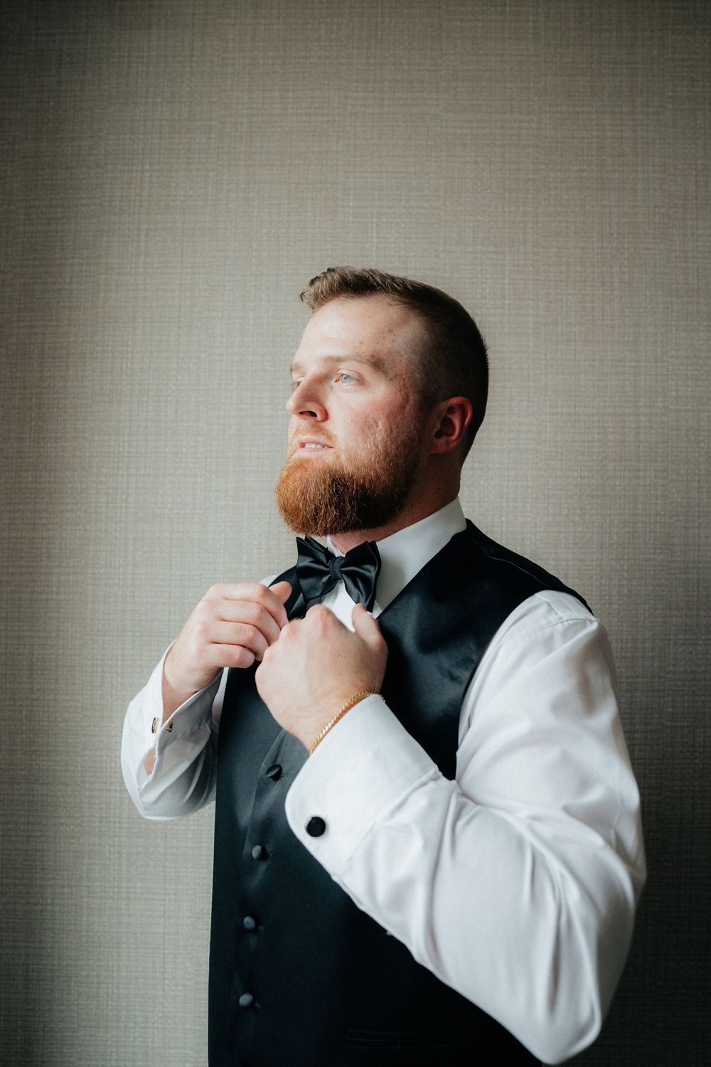 Sequence of a groomsman adjusting his bowtie against a grey backdrop.