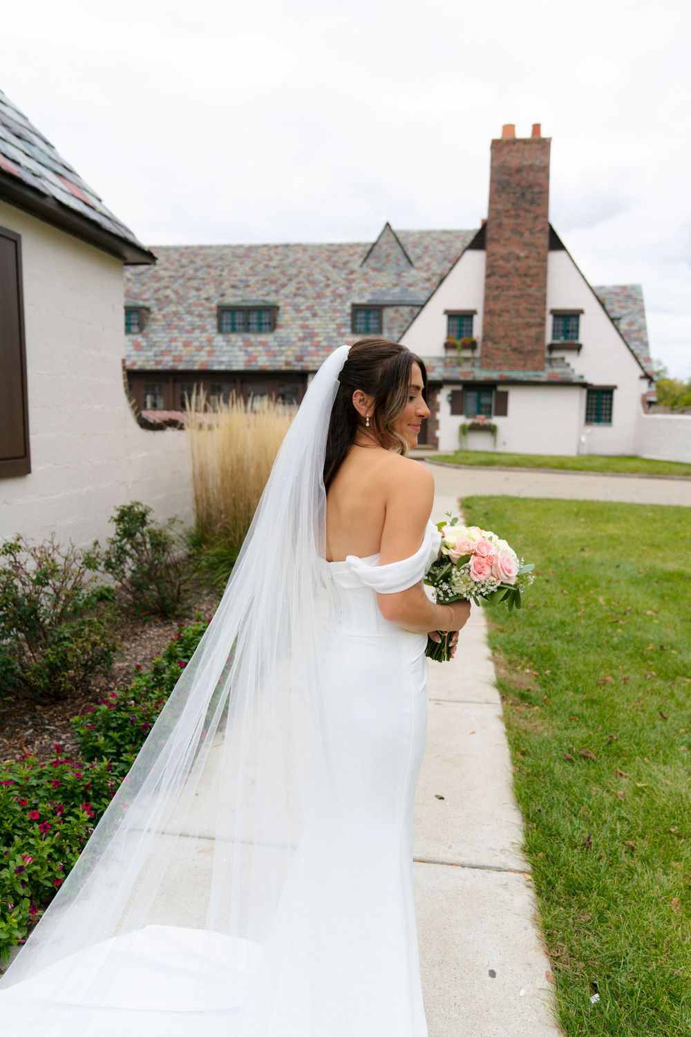 Flowing white wedding dress and veil captured from behind against architectural backdrop.