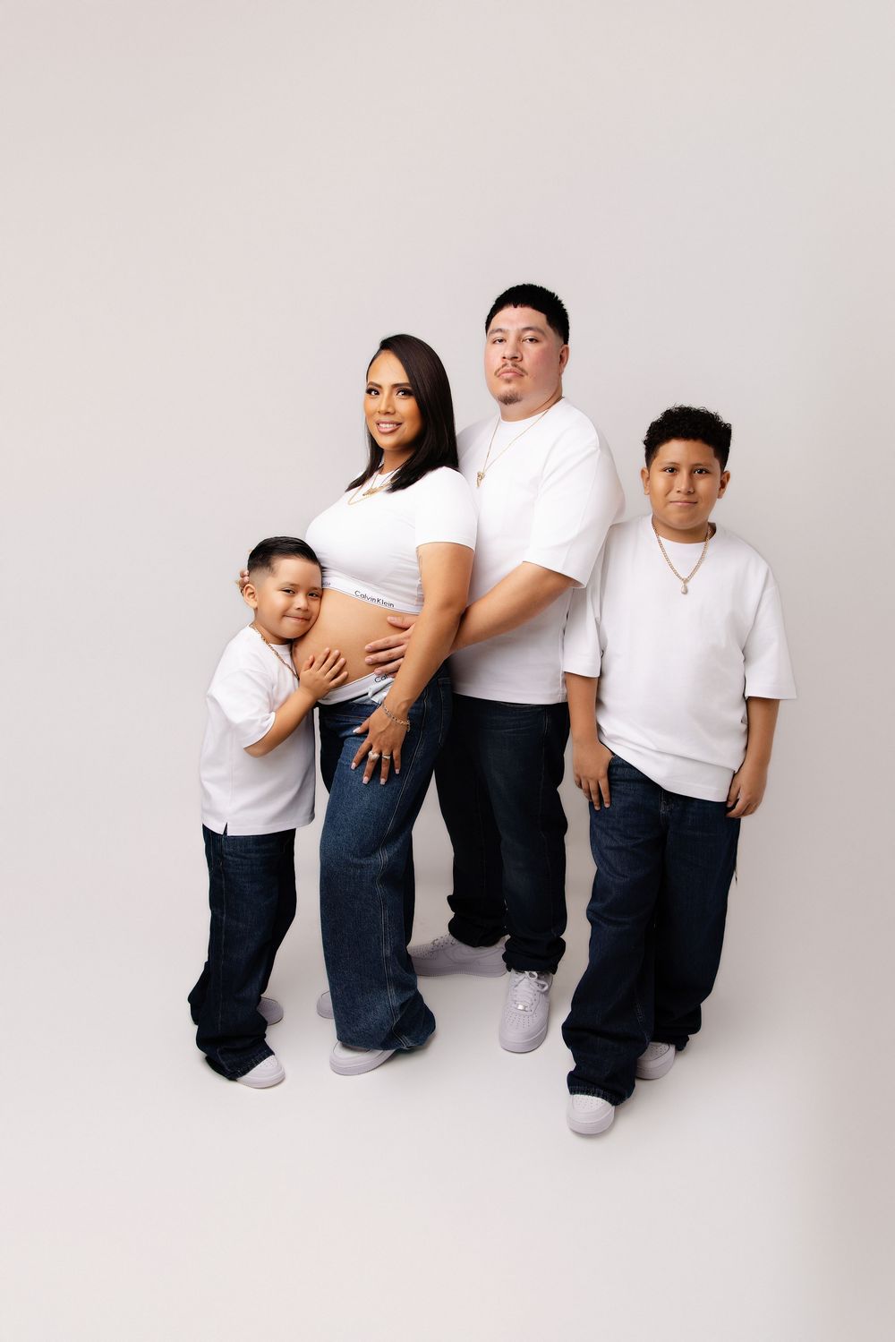 Family members wearing matching white t-shirts and dark jeans pose together in a minimalist studio setting.