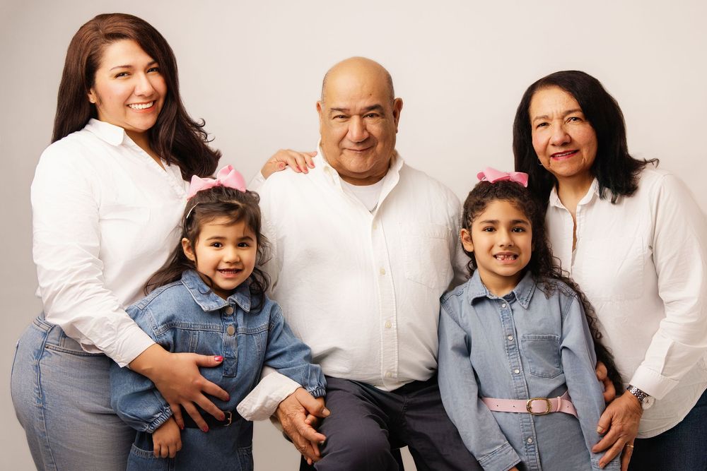 A family of five wearing coordinated white and denim outfits poses together for a warm studio portrait.