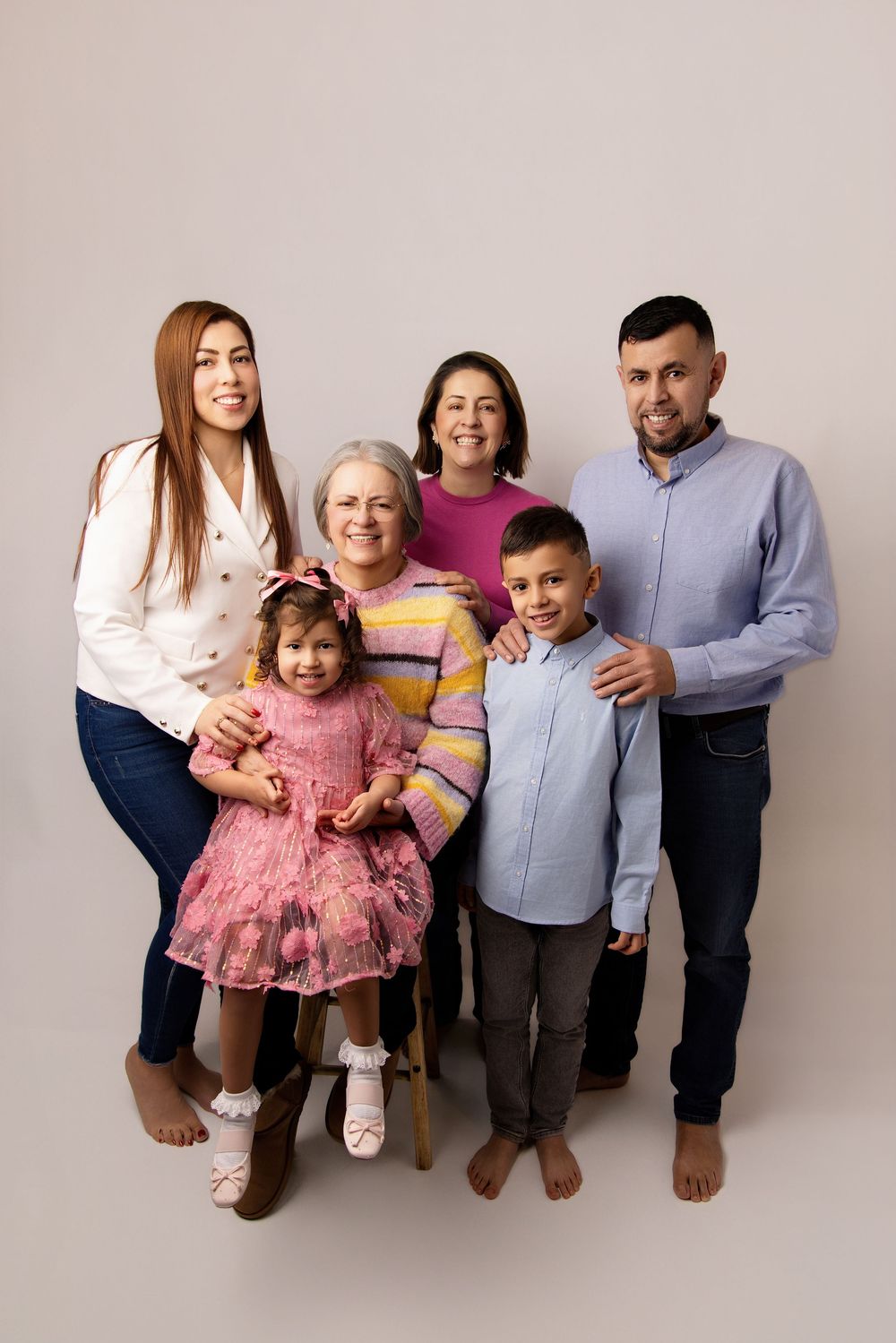 Multi-generational family poses together against neutral background wearing casual clothing in studio portrait setting.