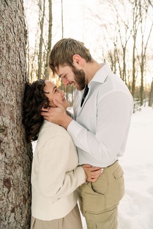 A romantic winter engagement photoshoot with a couple embracing against a snowy forest backdrop.