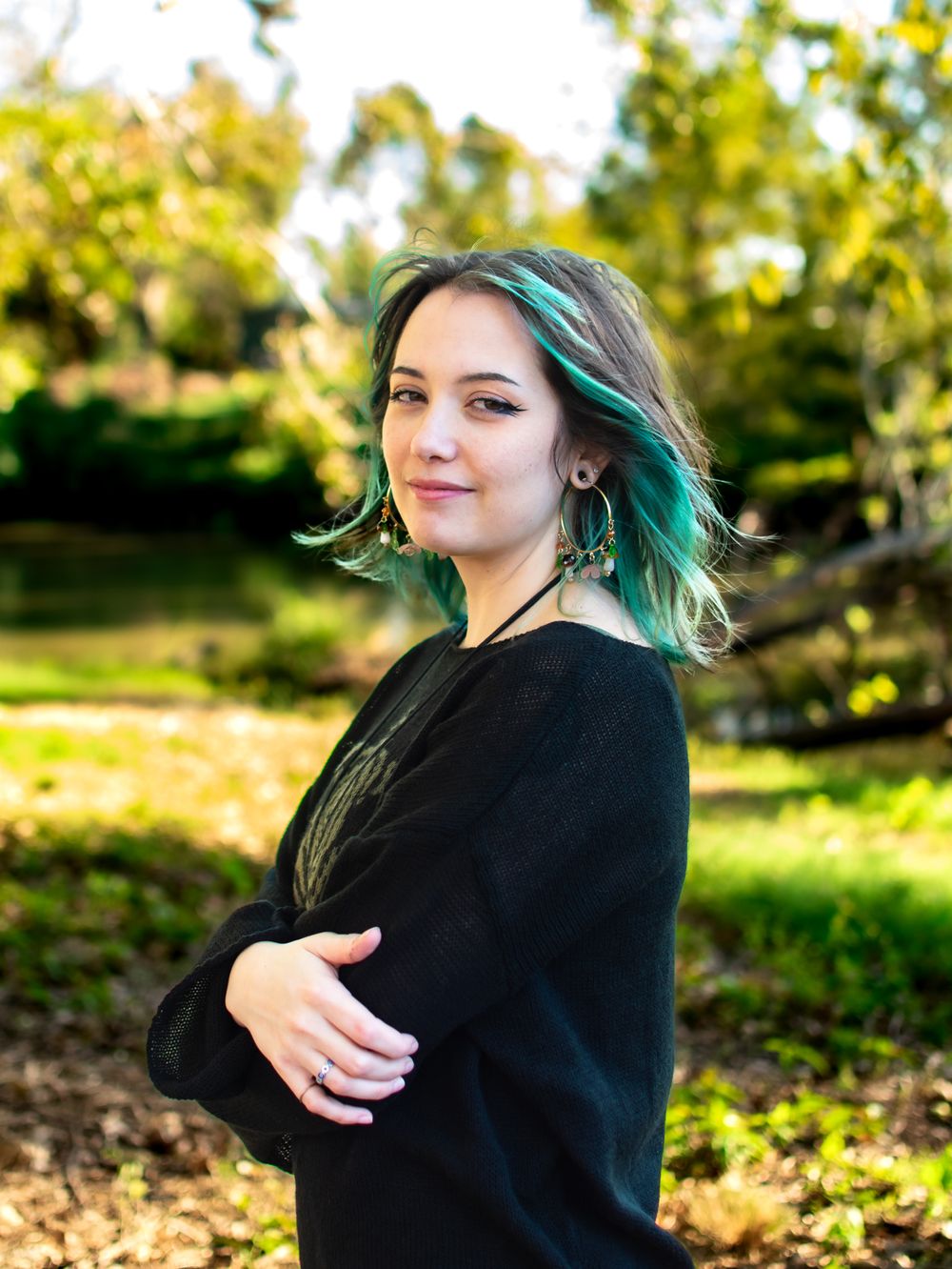 Side profile portrait featuring teal hair and black sweater against a nature backdrop.