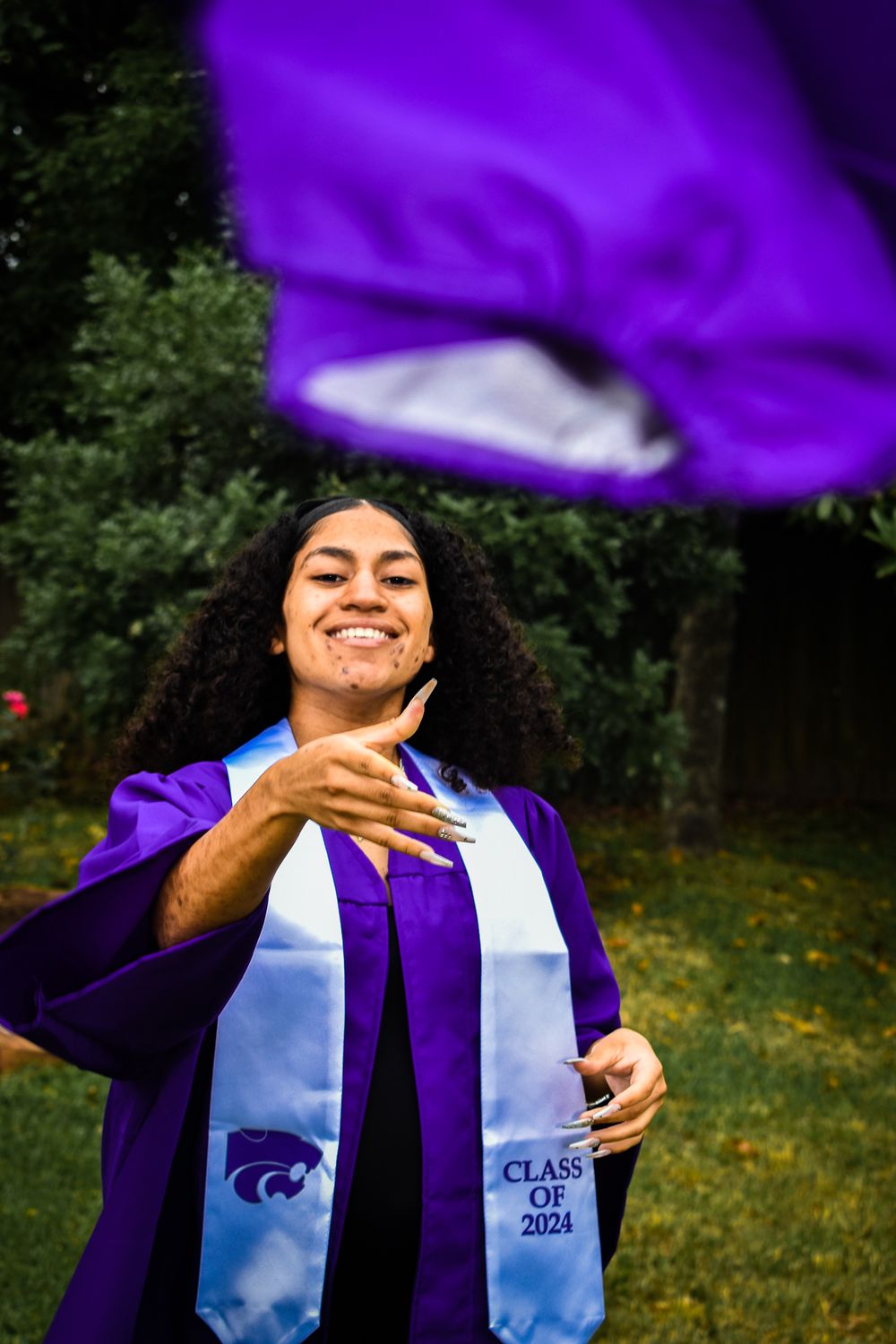 Graduate in purple cap and gown showing excitement during outdoor celebration.