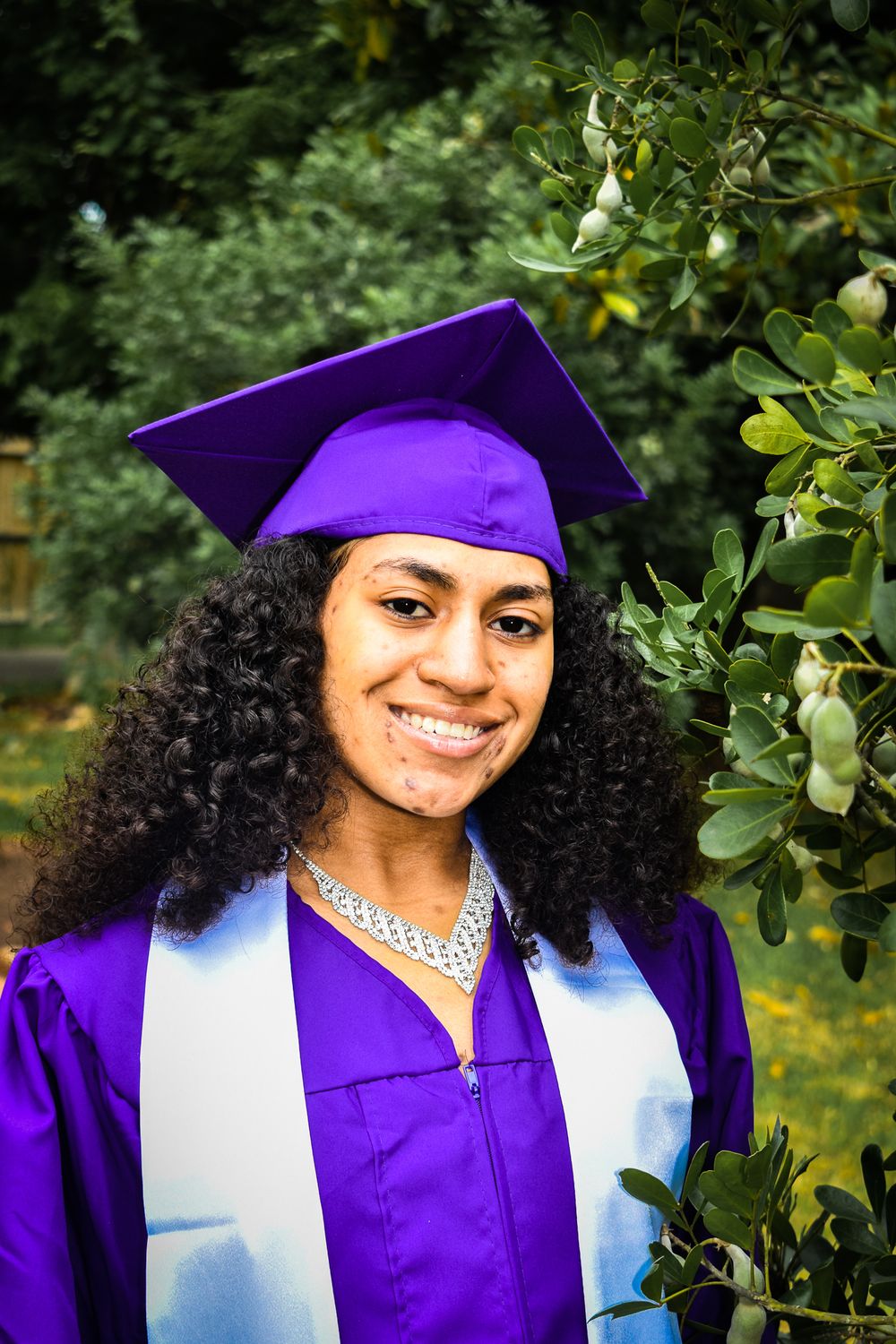 Kansas State University graduate in purple regalia photographed in garden setting.