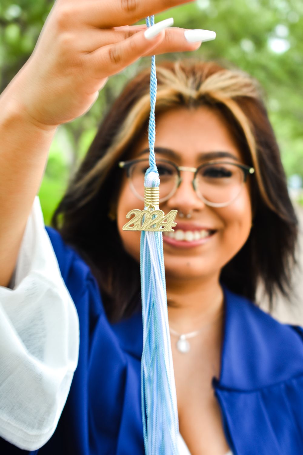 Close-up of graduation tassel being held up against green foliage background.