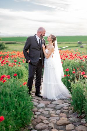 Wedding couple poses romantically in a field of vibrant red poppies and stone path at sunset.