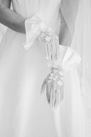 Delicate white bridal gloves adorned with small floral appliques against a light background.