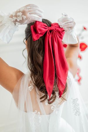 A white bridal veil and delicate red bow adorned to dark brown hair captured in a romantic style.