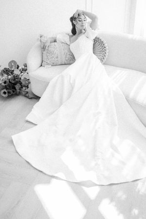 A flowing white wedding gown with ornate details laid out dramatically on a light floor in multiple artistic angles.