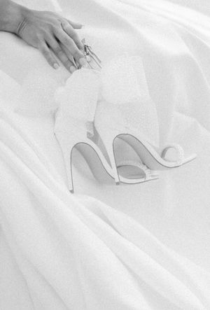 Wedding shoes sitting on white fabric with hands arranging them delicately.