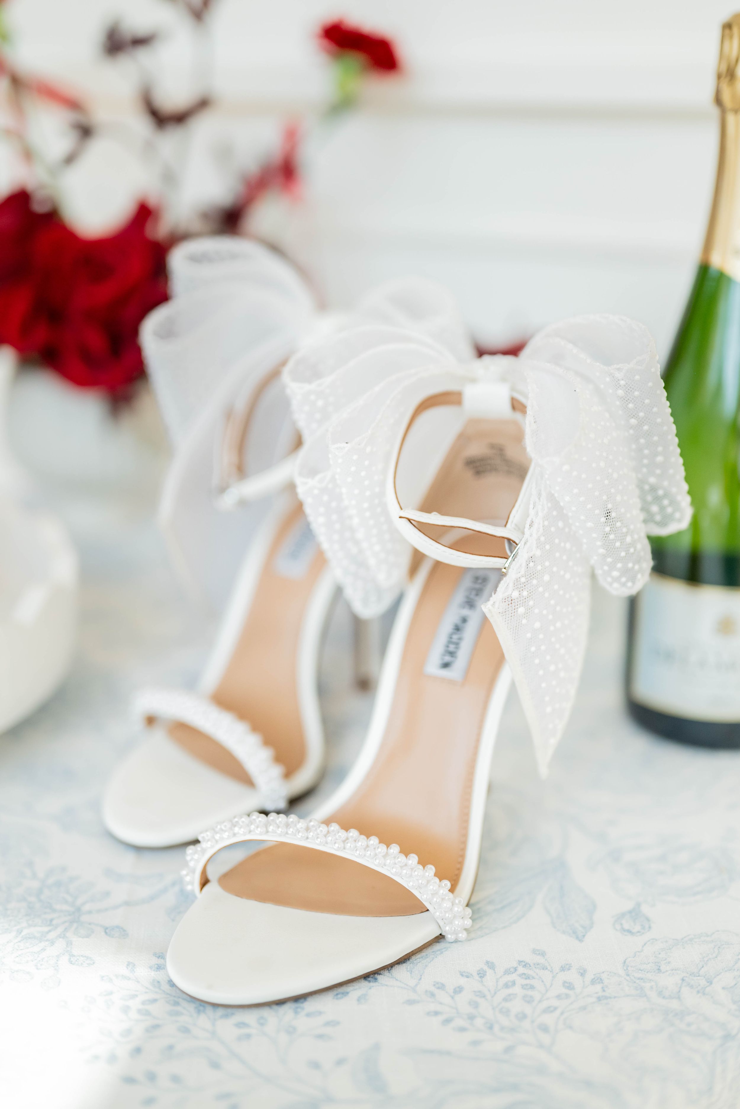 Elegant white lace wedding shoes with delicate bow details displayed on a lacy white surface.