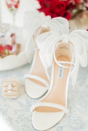 Elegant white bridal sandals with ankle straps and delicate details displayed on blue floral tablecloth.