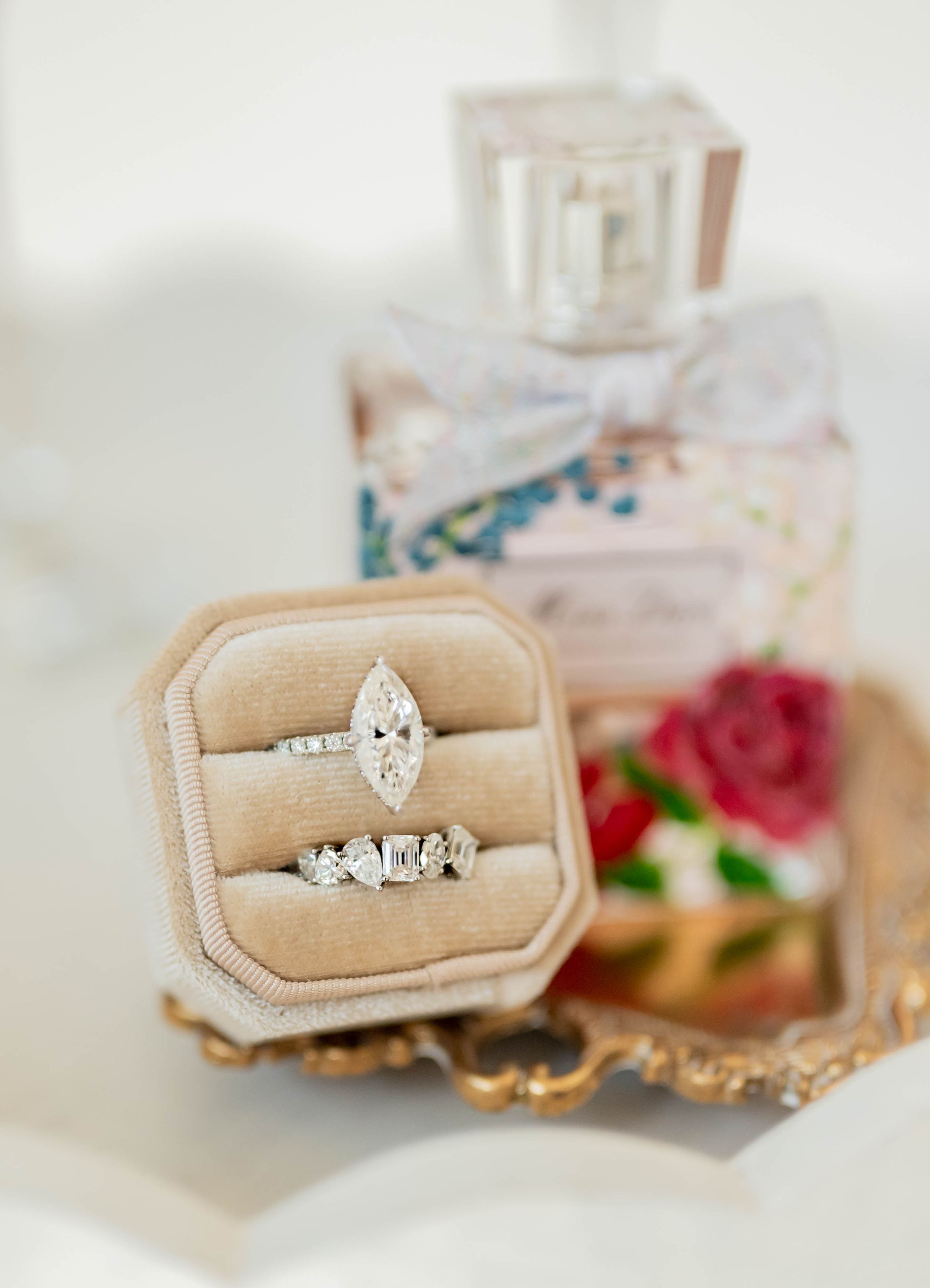 A vintage wedding ring displayed on a beige velvet ring box with rose decorations in the background.