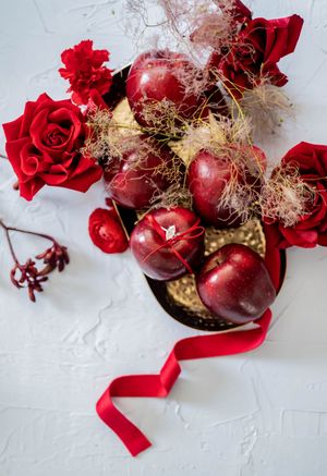 Fresh red apples decorated with red roses, baby's breath flowers and silk ribbon on white textured background.