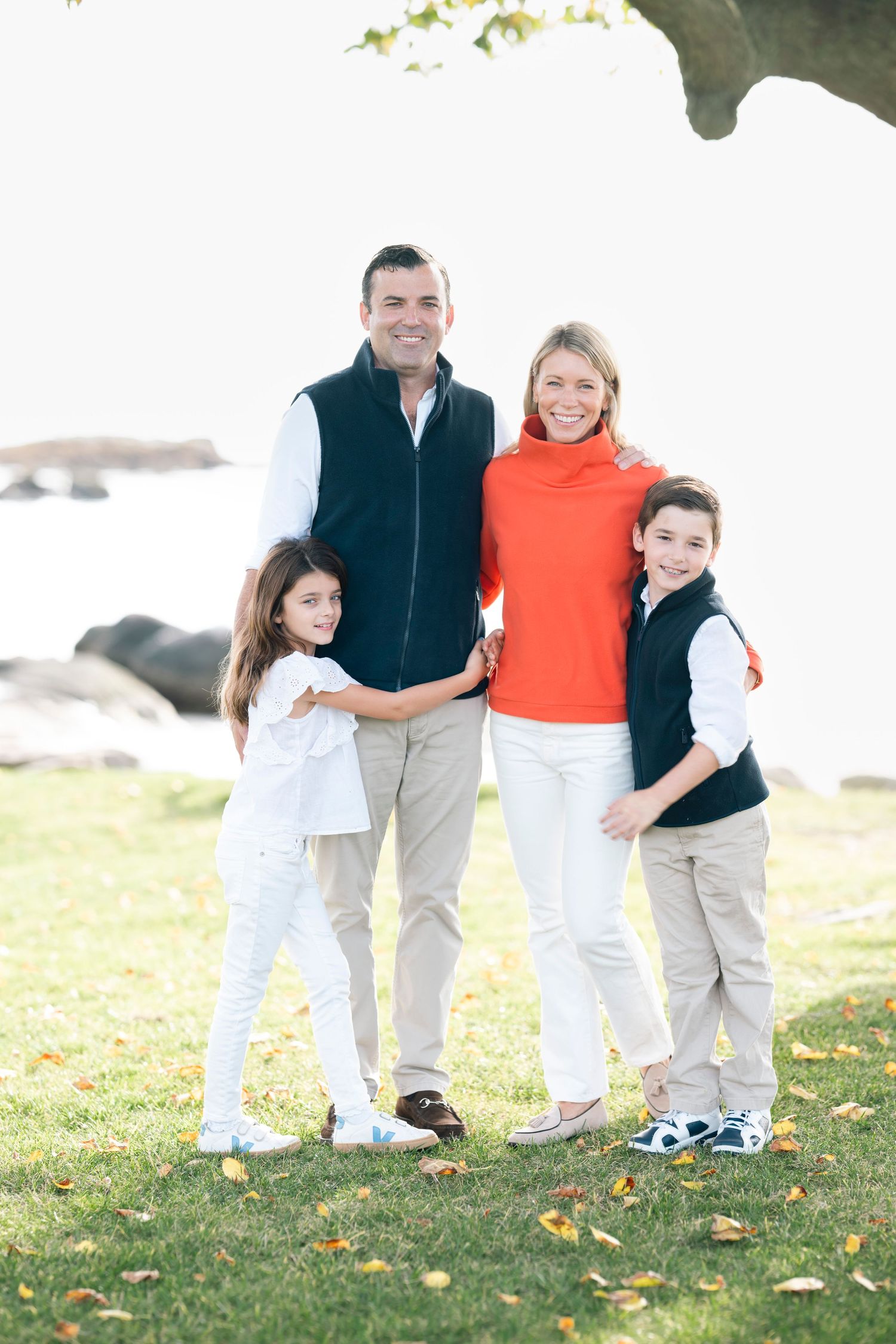 Family dressed in coordinating outfits poses together on grassy lawn near water.
