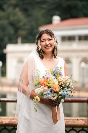 A radiant bride holds a colorful bouquet featuring orange and blue flowers against a classic backdrop.