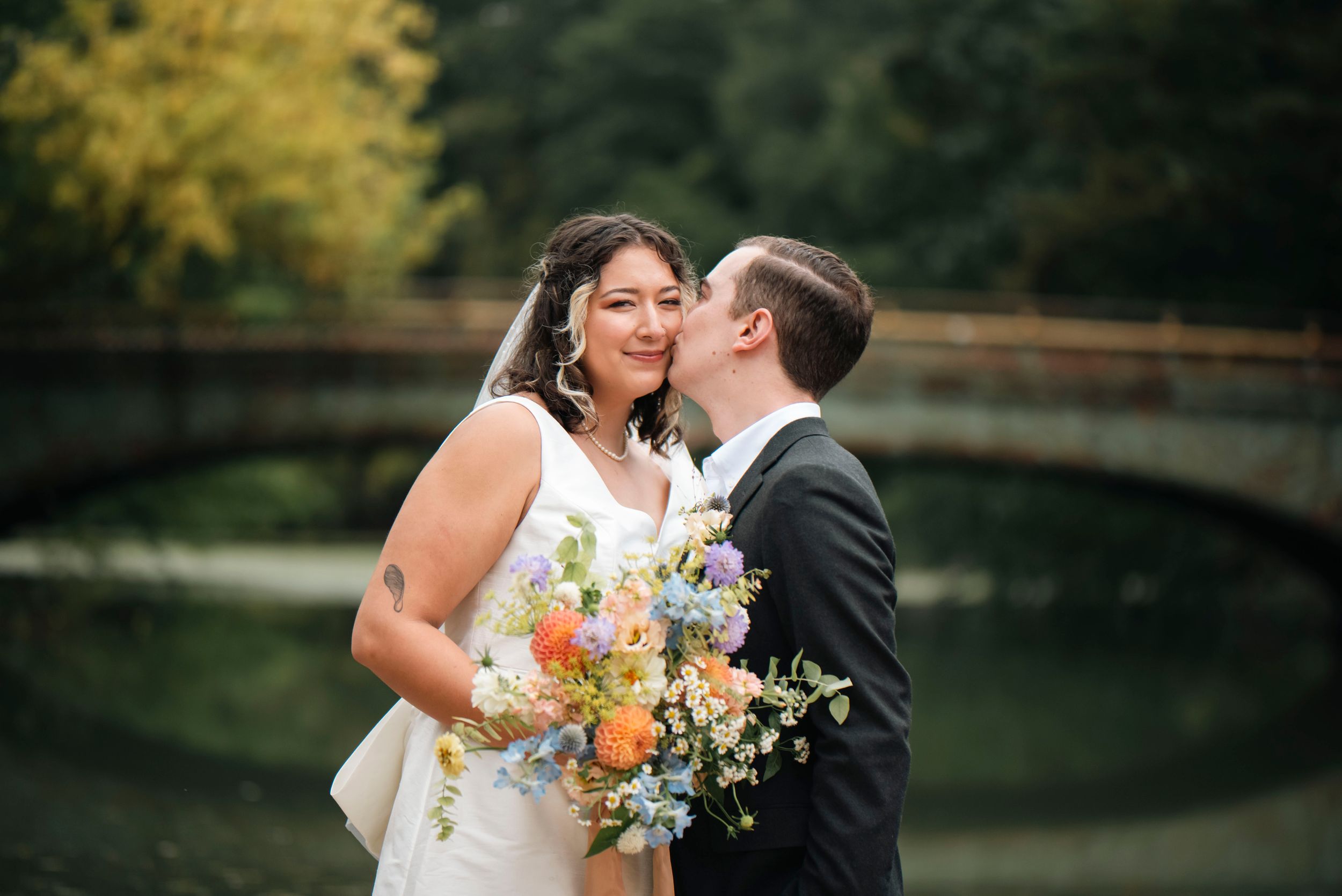 A romantic wedding moment captured with a stone bridge and autumn foliage in the background.