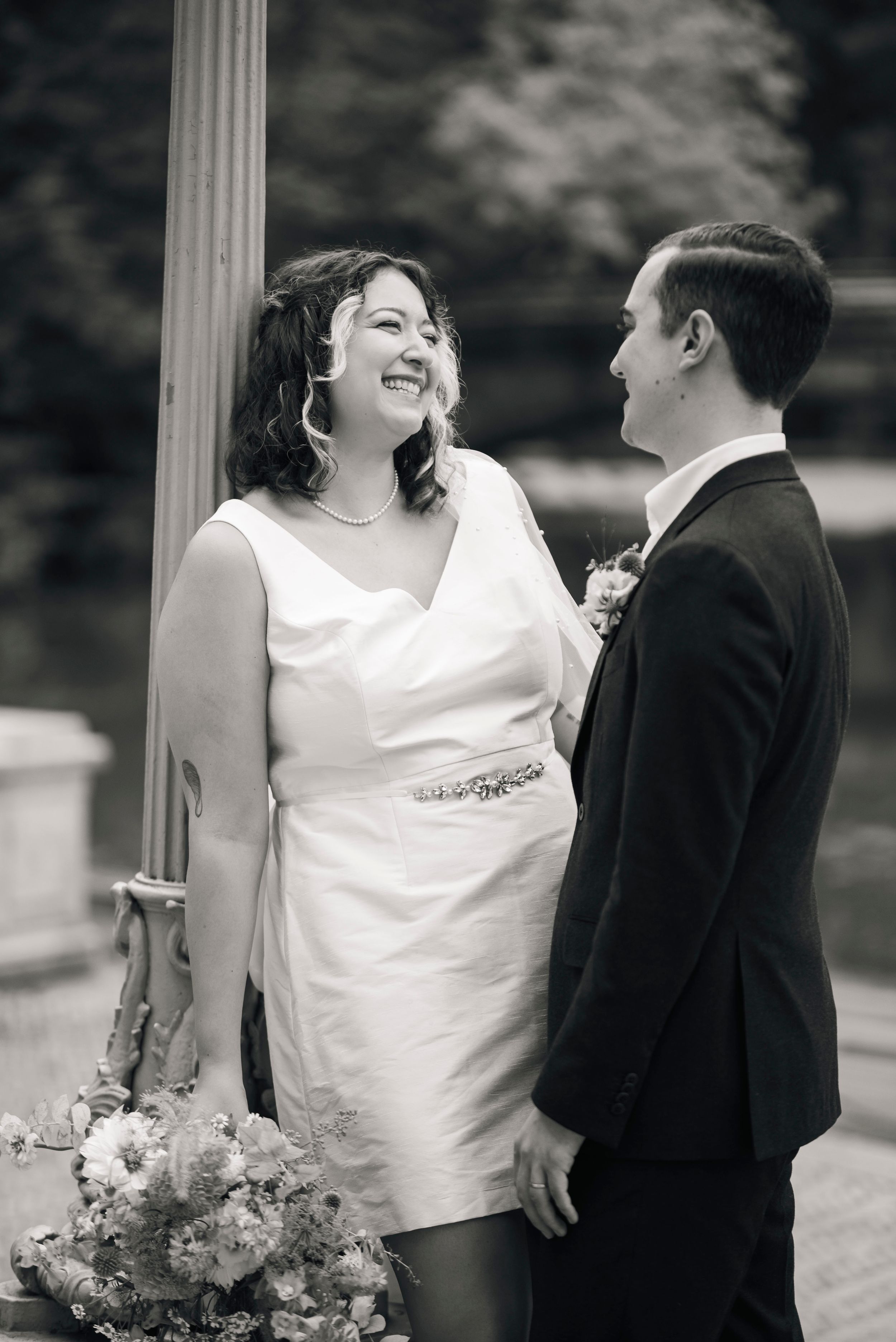 A black and white wedding portrait capturing a tender moment by a classic column.