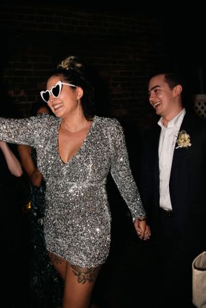 Couple at evening celebration with one wearing sparkly silver dress and heart sunglasses.