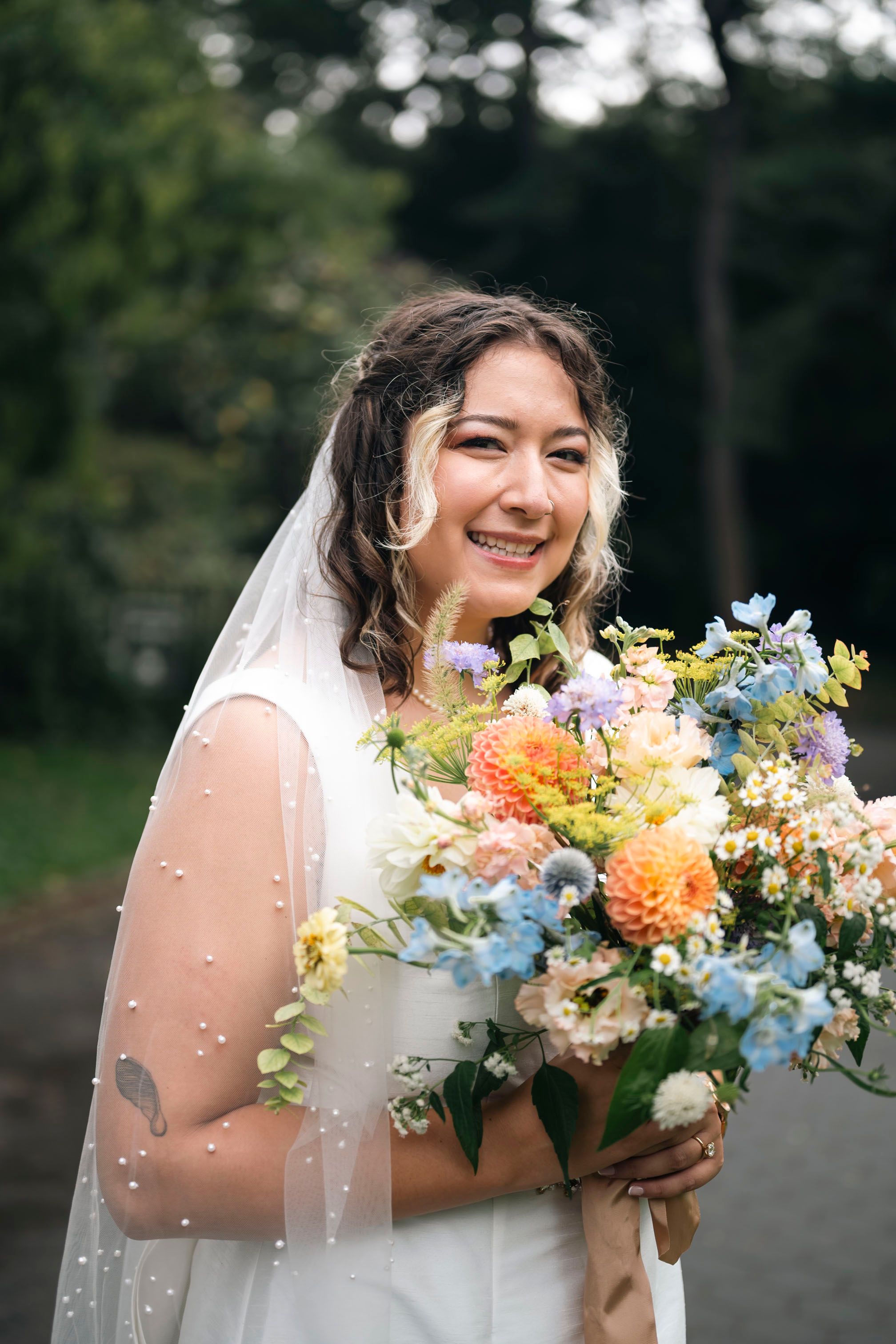 Colorful summer wedding bouquet with light blue, peach, and purple wildflowers complemented by a flowing veil.