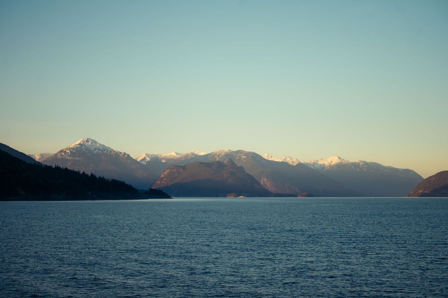 Serene mountain lake landscape with snow-capped peaks reflecting in calm blue water at dusk.

Vancouver Canada Scene