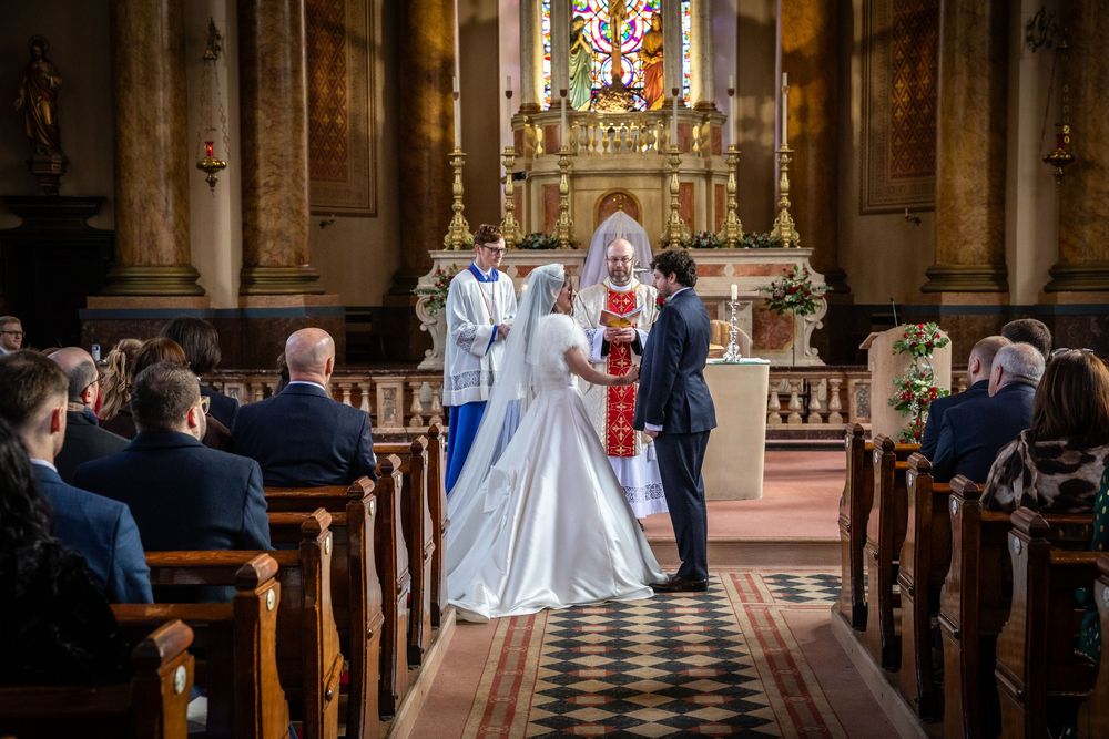 Bride and groom exchange vows at a church altar during a traditional wedding ceremony with guests seated in pews.