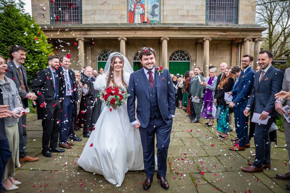 Bride and groom walk through confetti shower outside church after wedding ceremony.
