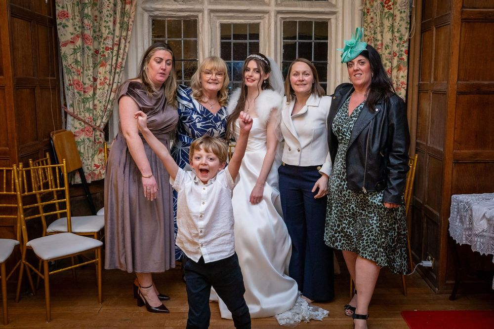 Bride poses with family and friends including an excited young boy at an elegant wedding venue.