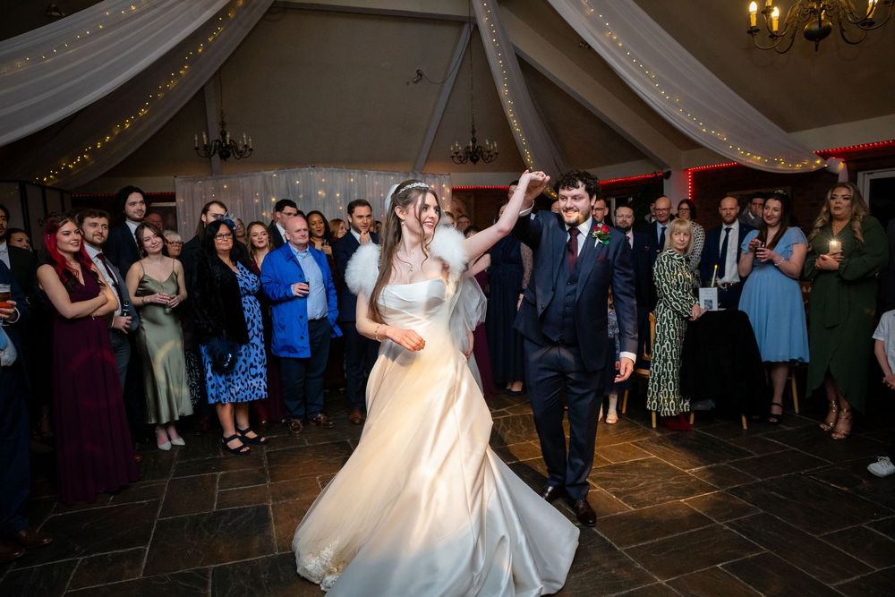 Bride and groom share first dance at wedding reception with guests watching in elegant venue.