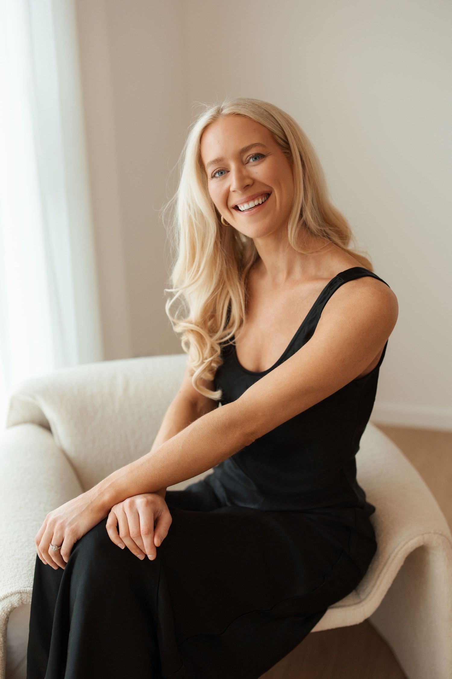 Blonde woman posing in a sleek black sleeveless maxi dress with thin straps against a white background.