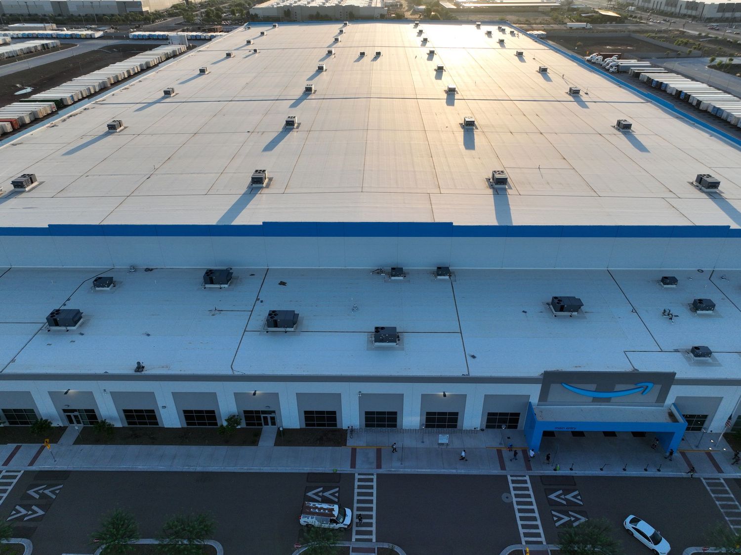 Aerial view of a large industrial warehouse facility with expansive rooftop solar panels and blue accented loading docks.