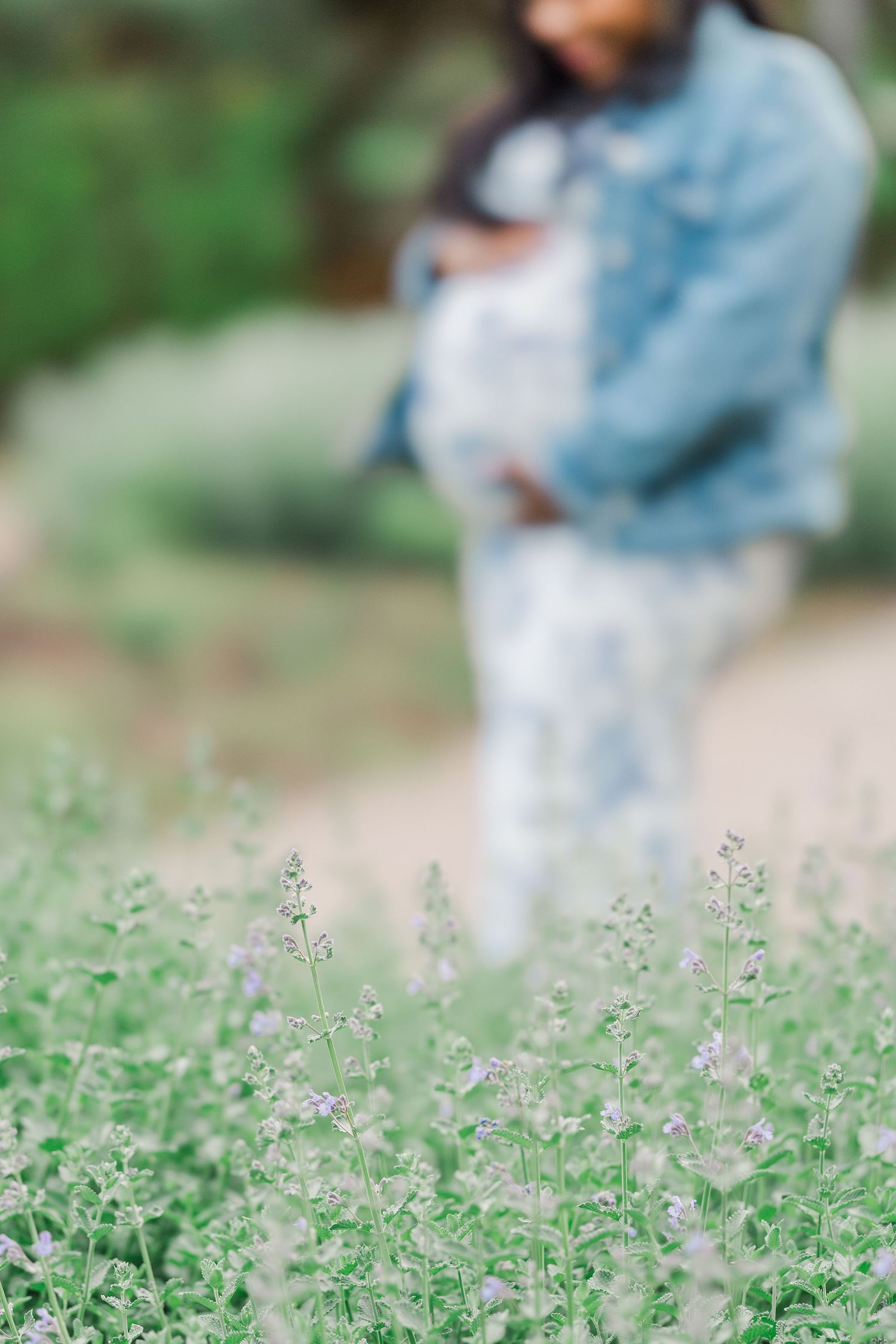 A woman in a denim jacket holds a baby among soft lavender wildflowers in a serene garden setting.