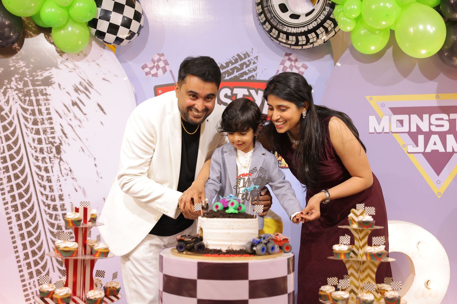 Family celebrating a Monster Jam themed birthday party with cake, balloons, and decorations.