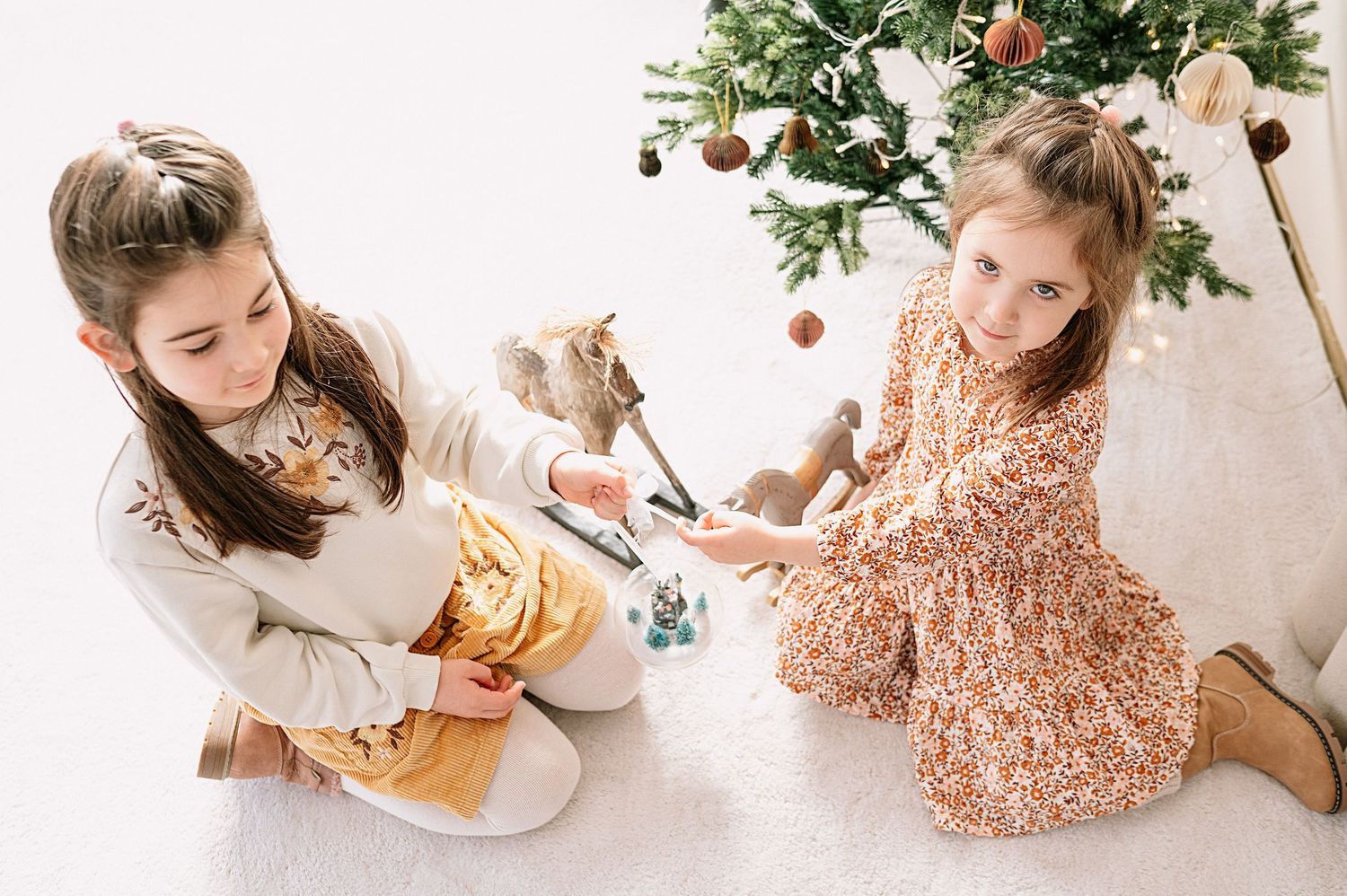 Zwei Mädchen spielen gemeinsam neben einem geschmückten Weihnachtsbaum.
