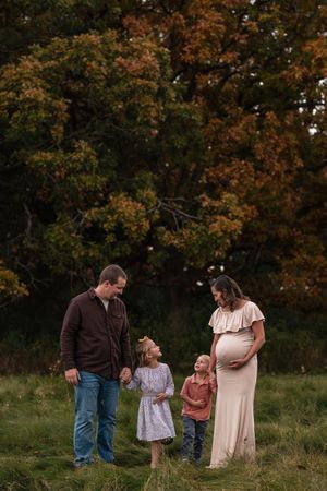 Pregnant woman in cream gown with family in autumn field, two children and husband smiling during maternity photo session.