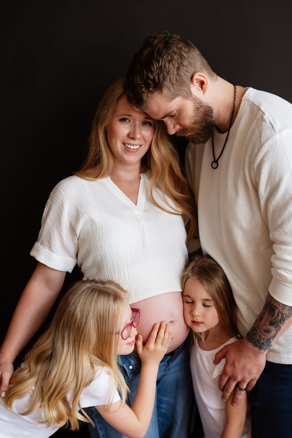 Happy pregnant woman with husband and two daughters touching baby bump in a family maternity photo session.