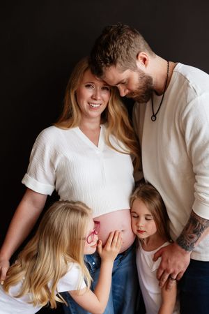 Happy pregnant woman with husband and two daughters touching baby bump in a family maternity photo session.