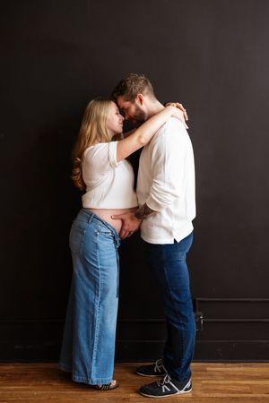 A couple in casual denim and white tops share an intimate embrace against a dark wall on a wooden floor.