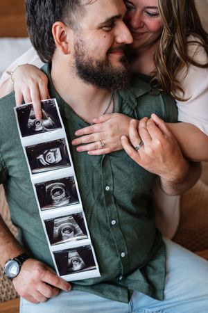Happy couple holding ultrasound photos, smiling and embracing, celebrating pregnancy announcement together.