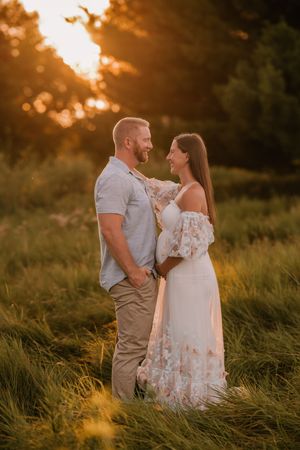 Couple sharing a romantic moment in a sunlit field during golden hour, woman in floral dress, man in casual attire.