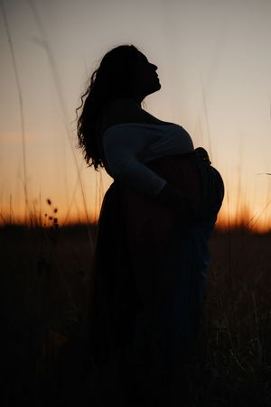 Silhouette of a pregnant woman cradling her belly at sunset in a field of tall grass.