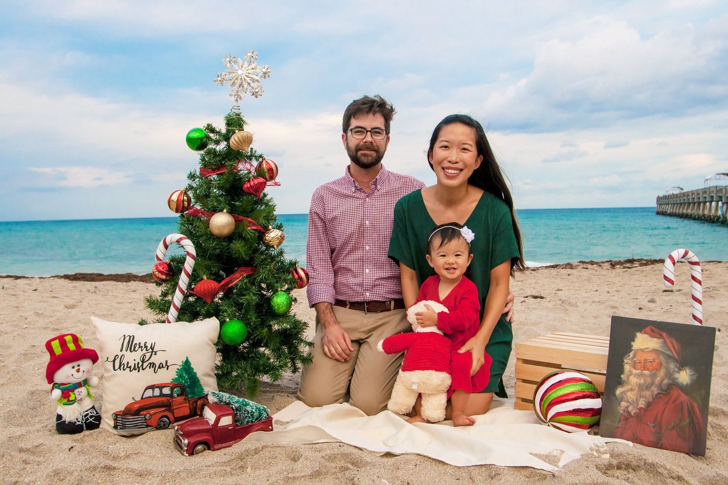 Christmas mini on the beach at lake worth beach pier family smiling with daughter and small Christmas decor by Photogenic Fox Photography