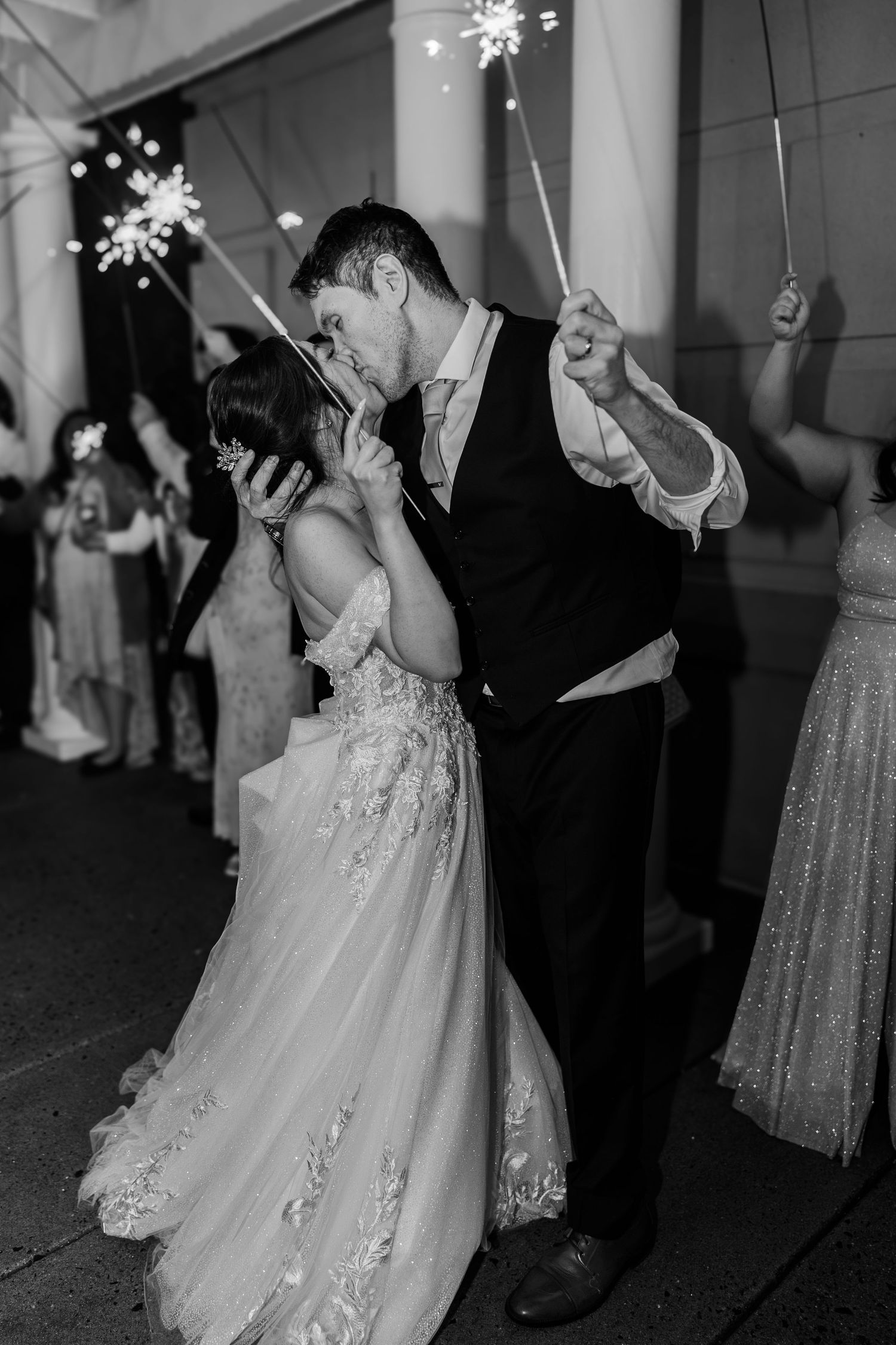Black and white photo of a bride and groom sharing a kiss during a sparkler send-off at their wedding reception.
