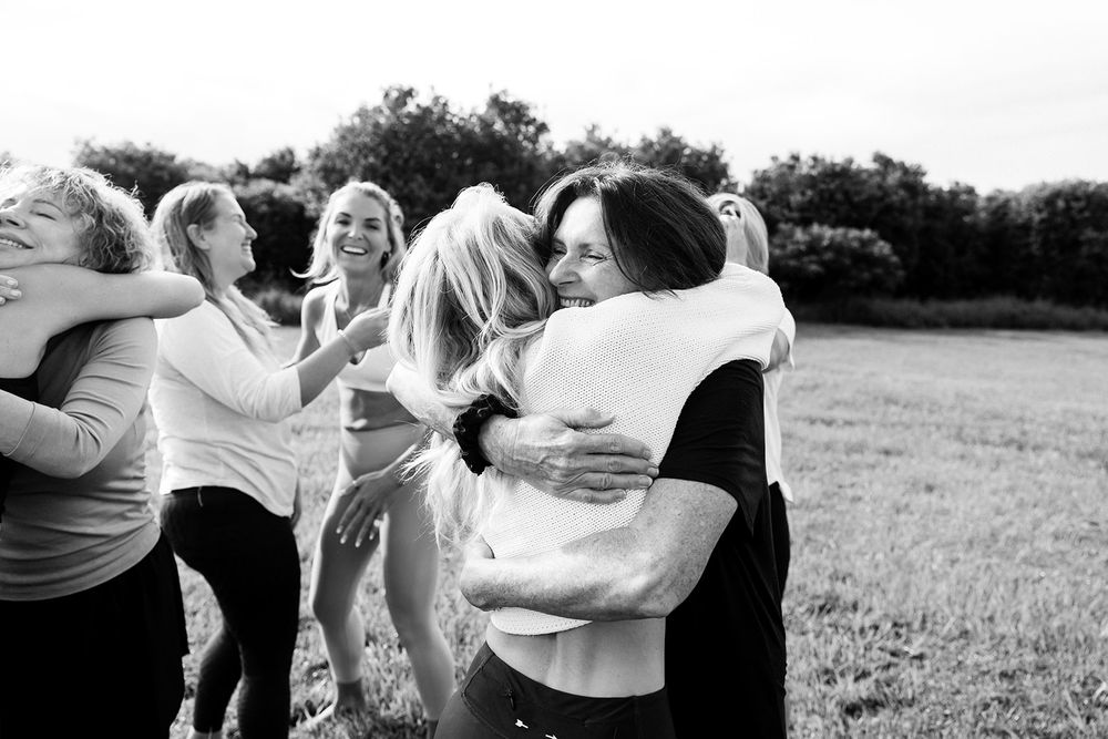 Group of women hugging and laughing together outdoors in a field, black and white photo.